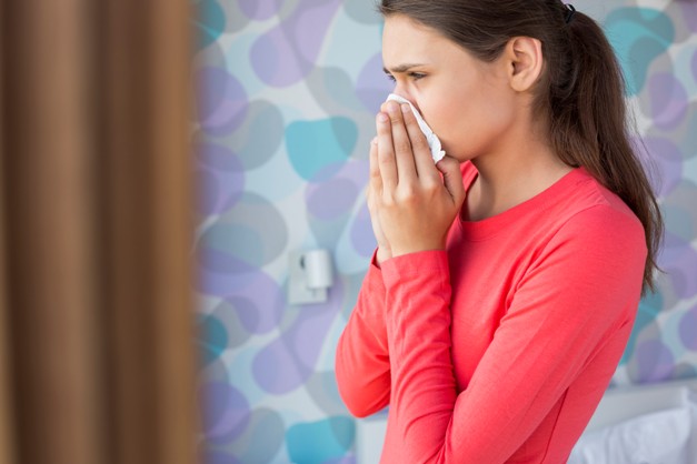 Side view of young woman blowing nose at home